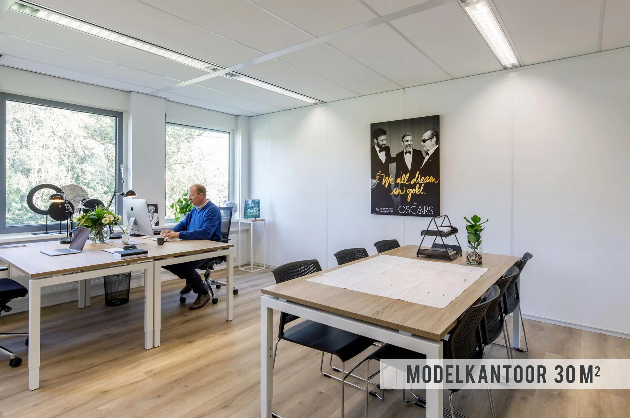 Modern ingericht modelkantoor van 30 m² met werk- en vergadertafels, grote ramen en een man die aan een bureau werkt.